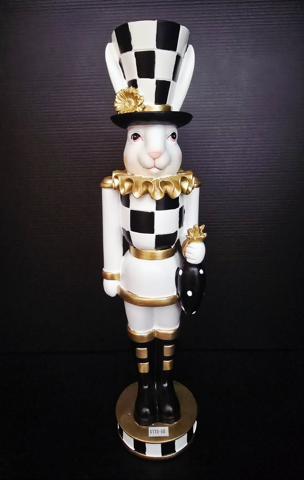 Decorative rabbit figurine in a checkered outfit with a black and white hat on a dark background