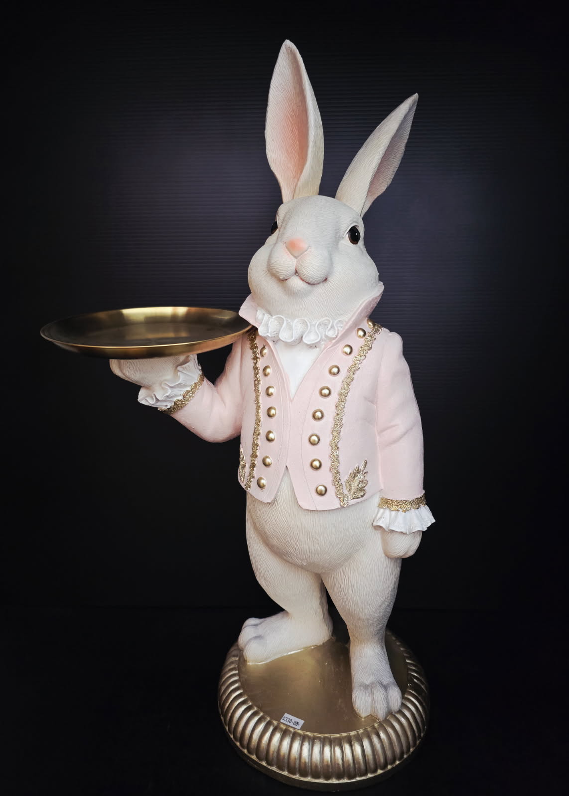 Decorative rabbit figure in a suit holding a gold tray on a black background