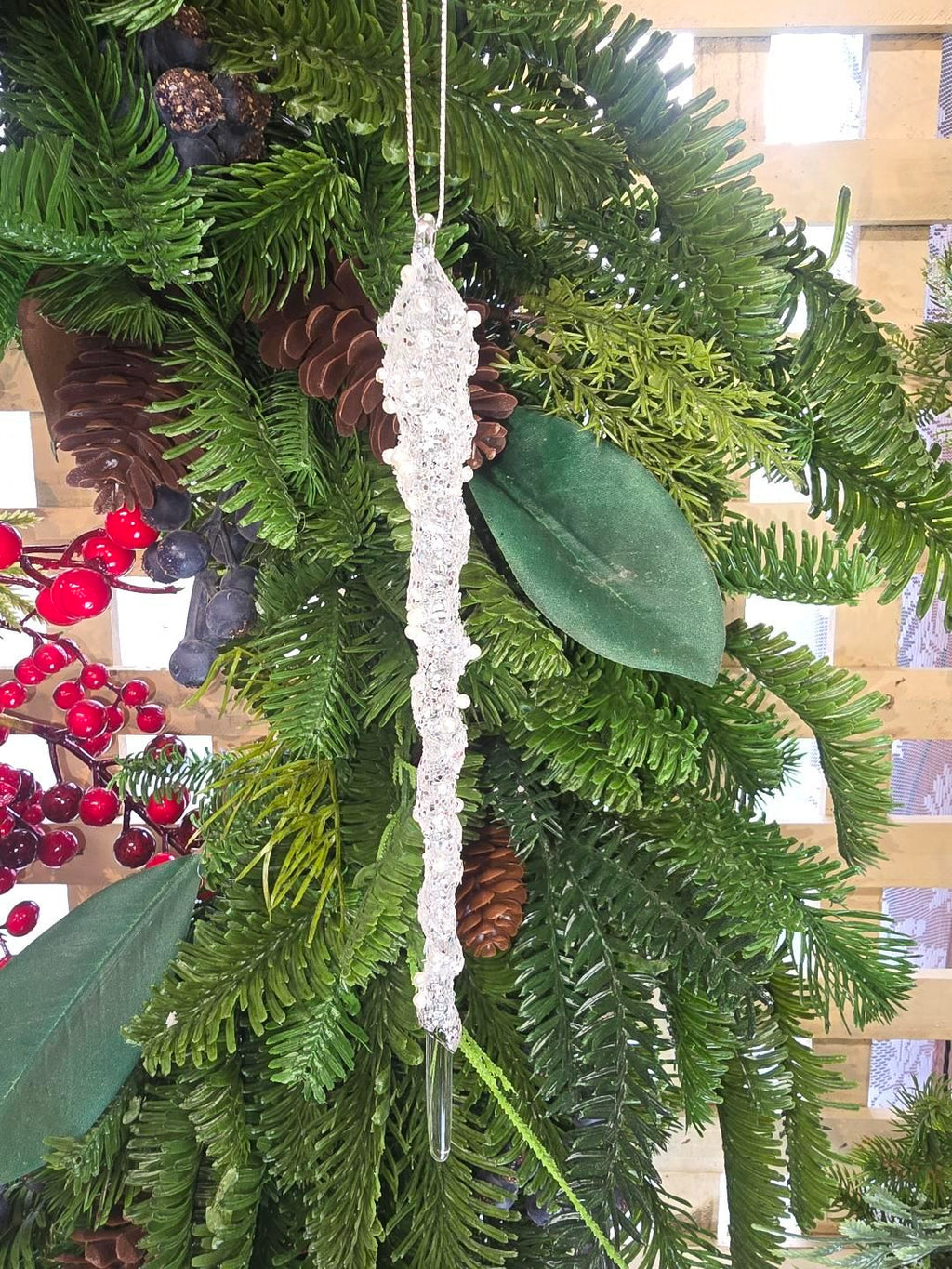 Pearl and crystal encrusted icicle ornament hanging on a Christmas tree decorated with pine cones, red berries and magnolia leaves, showing the full length and dense beaded texture