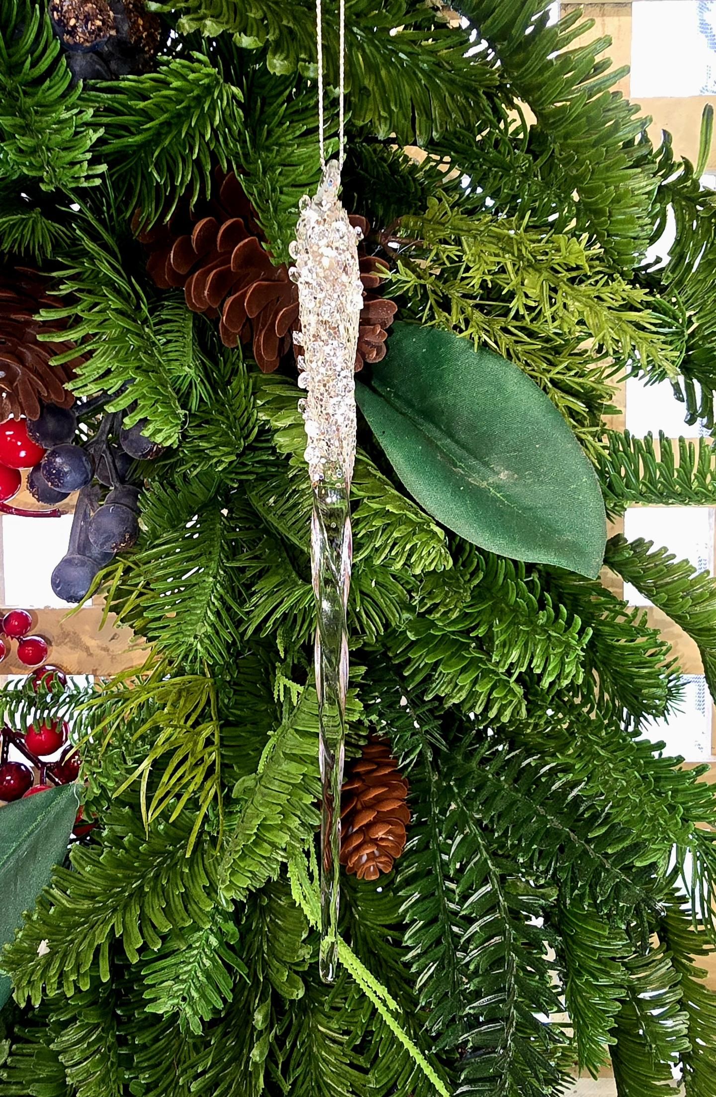 Close-up of the Encrusted Icicle ornament nestled in a pine and pinecone wreath, showing the spiral-twisted glass body and sparkling crystal-bead top