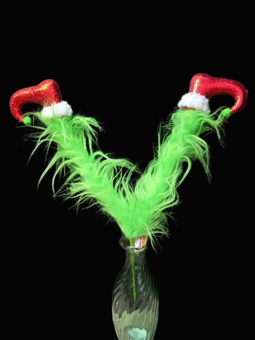 Decorative item with green feathers and red hats in a glass bottle against a black background