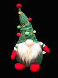 Sitting Christmas gnome decoration with a green hat and red shoes, styled on a dark background for cozy festive shelf decor