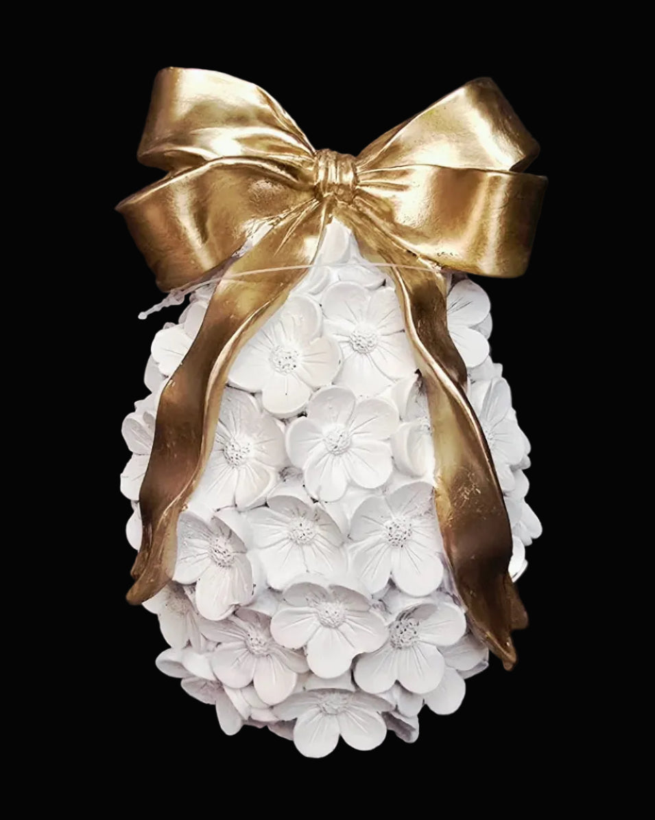 Decorative item with white flowers and a gold bow on a black background