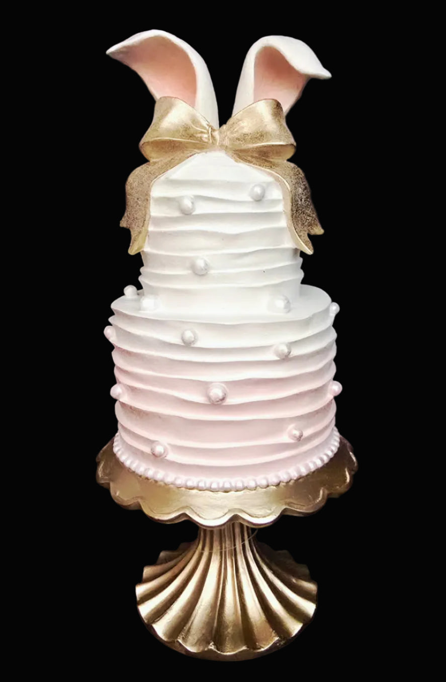 Decorative faux tiered Easter cake with sculpted bunny ears, glittered gold bow and white pearl dot embellishment on gold scalloped stand, on black background — 40.5cm high — Mistletoe Home