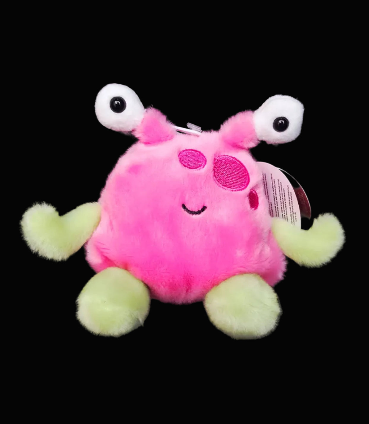 Plush toy with pink body and green legs on a dark background