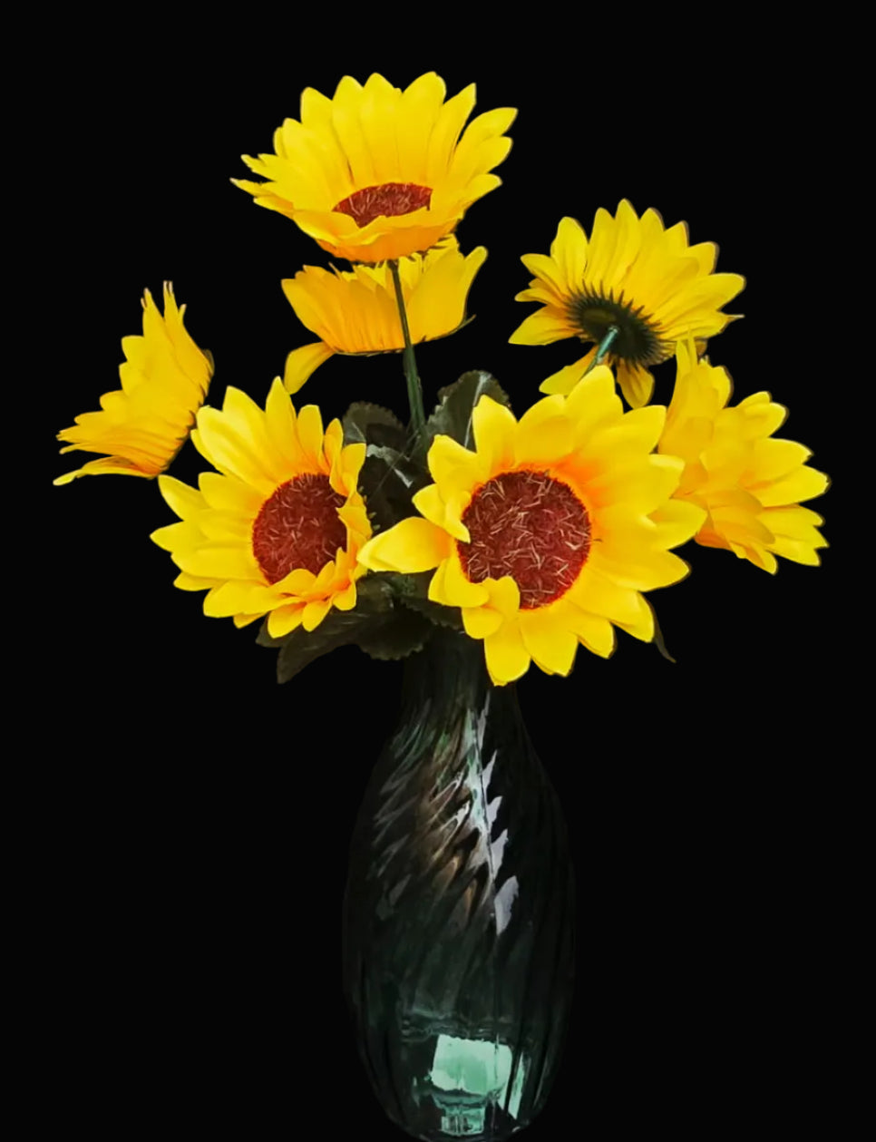 Faux sunflower bunch with 7 yellow blooms and russet brown centres with green foliage in a green glass vase on black background — Mistletoe Home
