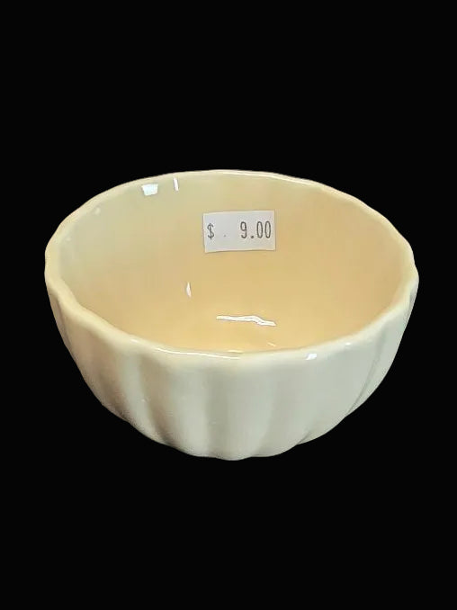 Beige ceramic bowl on a dark surface with a price tag attached.