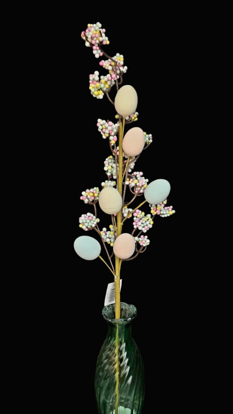 Decorative arrangement with pastel-colored eggs and flowers in a green vase against a dark background