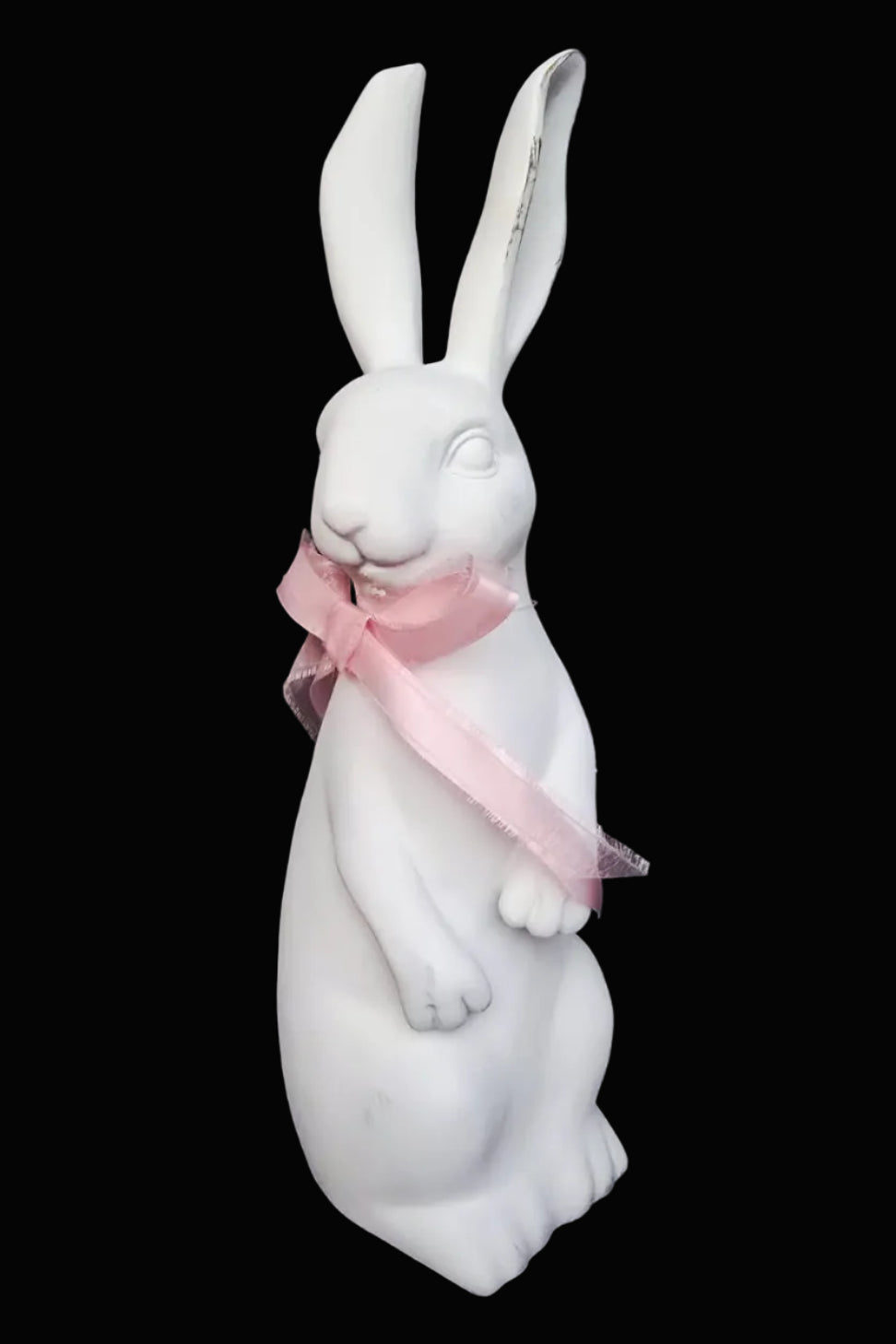 White ceramic rabbit figurine with a pink bow on a dark background