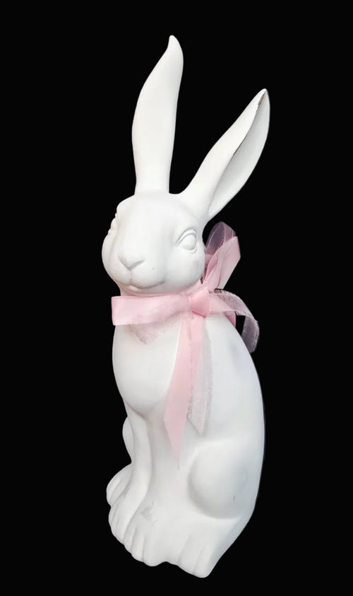 White rabbit figurine with a pink bow on a dark background